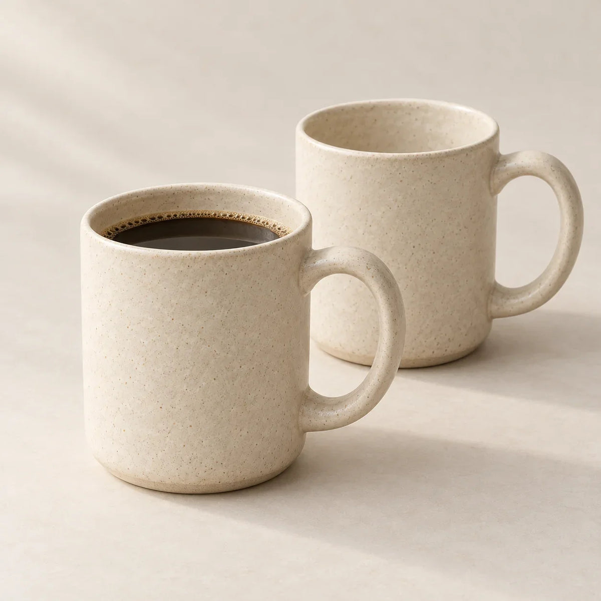 Two ivory ceramic mugs, one filled with coffee